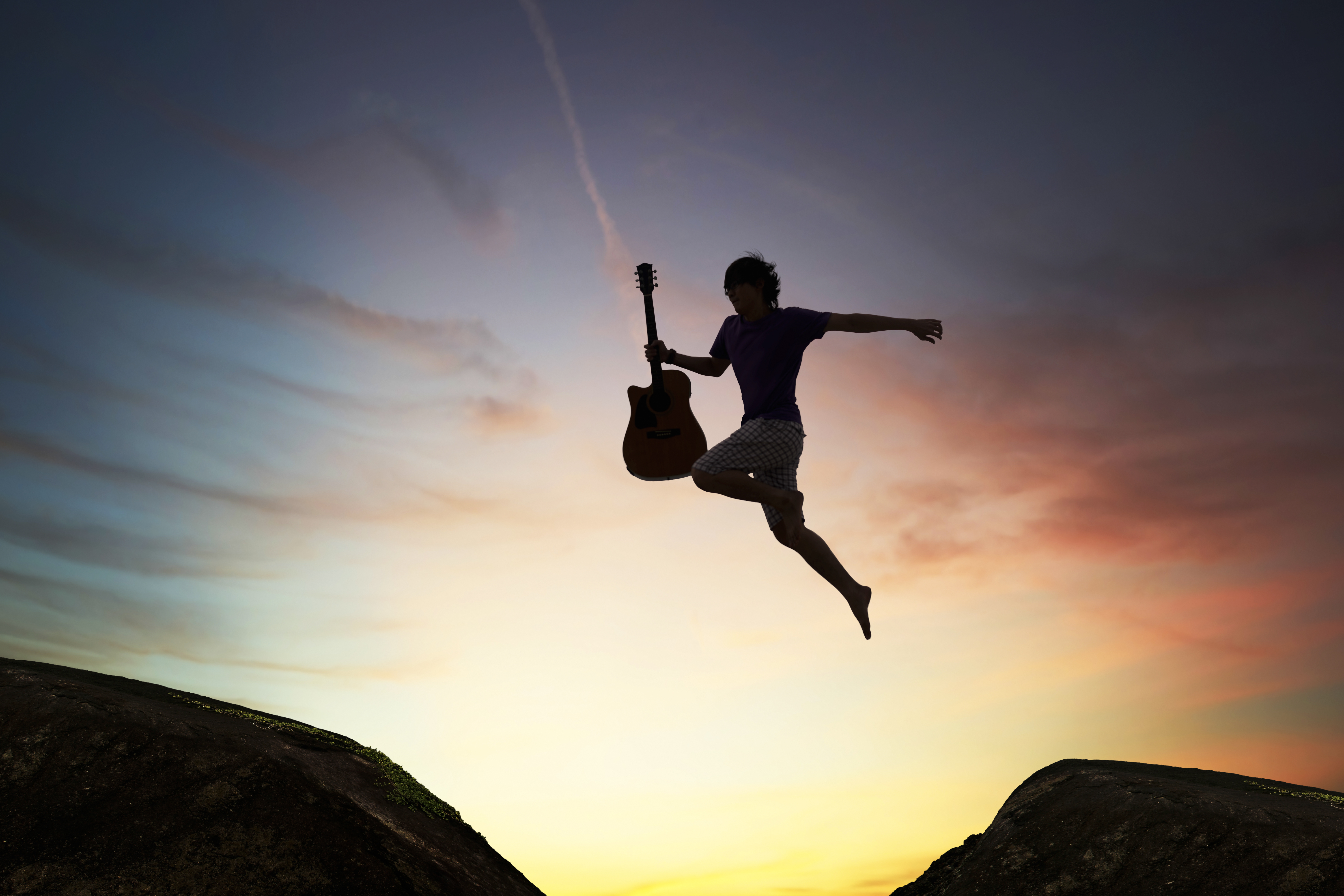 silhouette of brave guy holding the guitar jumping through the gap,inspiration and success concept.